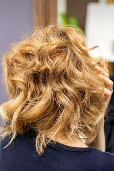 Rear view of young woman checking her new curly brown hairstyle at the hairdresser salon