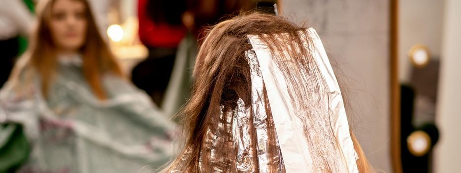 Beautiful young caucasian woman with foil in her hair while dyeing her hair sitting in a beauty salon