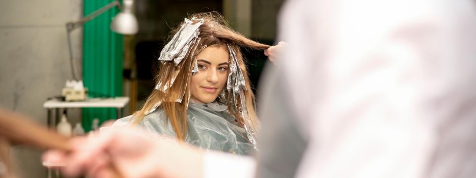 Portrait of a beautiful young caucasian woman who is smiling getting dyeing her hair with foil in a beauty salon