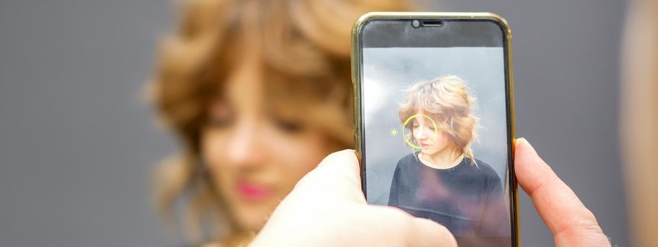 Man hairdresser taking pictures on the smartphone of her client's hairstyle against a gray background