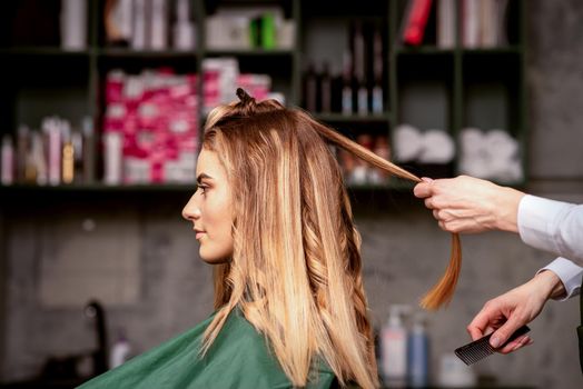 Professional hair care. Beautiful young caucasian blonde woman with long hair receiving hairstyling in a beauty salon