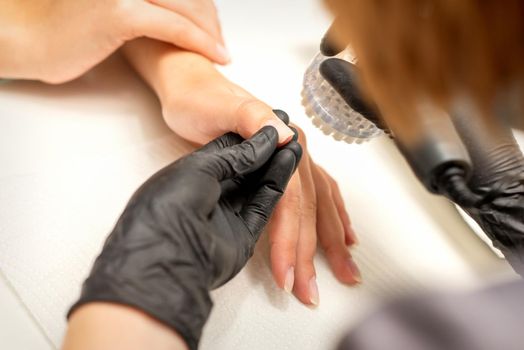 Hands of the manicure master removing dust from nails with a brush cleaning nails in a nail salon