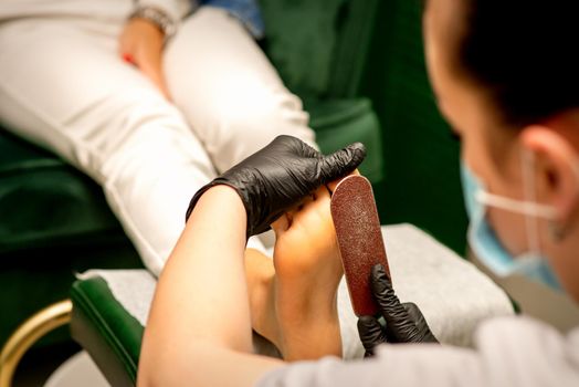 Pedicurist rubbing heel with a special grater on pedicure treatment in a beauty salon