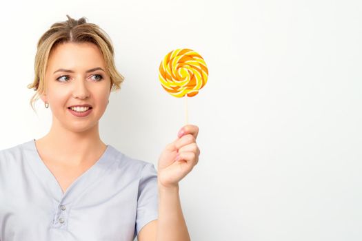 Waxing, depilation concept. The beautician is wearing a medical coat holding a sugar lollipop on white background