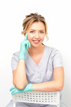 Close-up portrait of young smiling female caucasian healthcare worker sitting and staring at the camera wearing gloves on white background