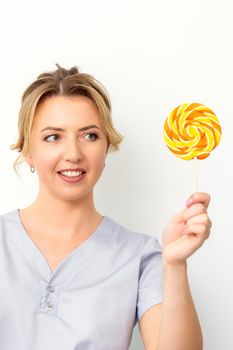 Waxing, depilation concept. The beautician is wearing a medical coat holding a sugar lollipop on white background