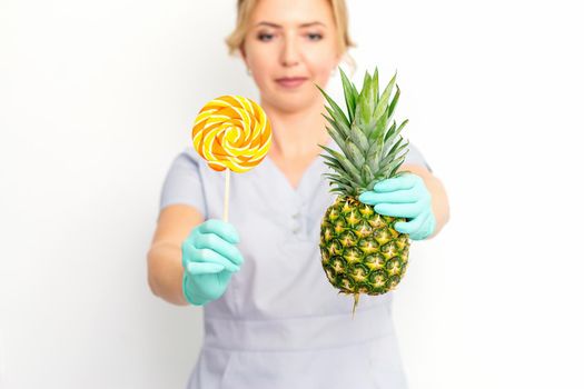 Young caucasian female doctor nutritionist holding fresh pineapple with lollipop over white background