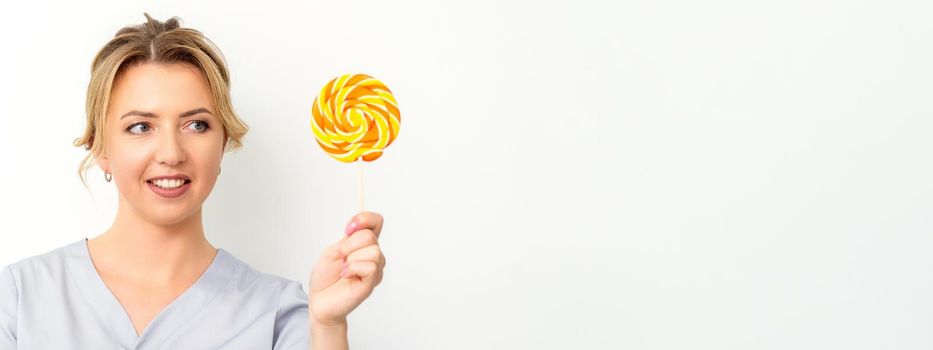 Waxing, depilation concept. The beautician is wearing a medical coat holding a sugar lollipop on white background