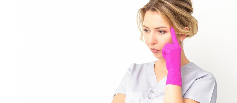 Young caucasian female doctor wearing gloves thoughtful looking away isolated on white background