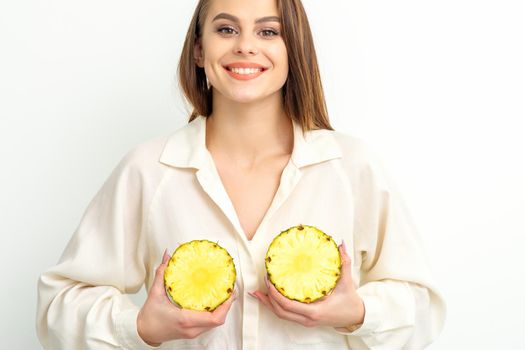 Young Caucasian smiling woman holding slices pineapple over white background, breast health concept