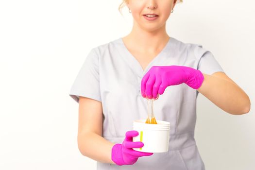 Portrait of a female caucasian beautician holding a jar of sugar paste for sugaring wearing pink gloves on white background