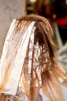 Beautiful young caucasian woman with foil in her hair while dyeing her hair sitting in a beauty salon