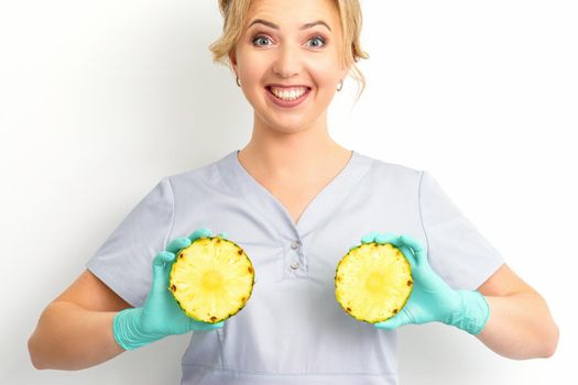 Young Caucasian smiling woman doctor nutritionist holding slices pineapple over isolated white background, breast health concept