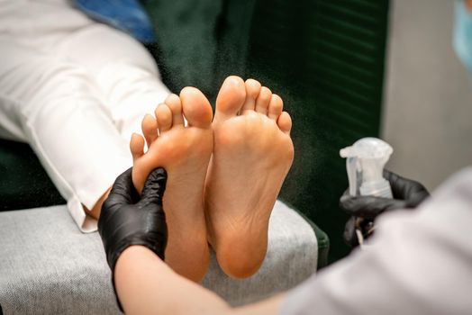 A woman getting a pedicure and pedicurist moisturizing female feet with lotion spraying in a beauty salon