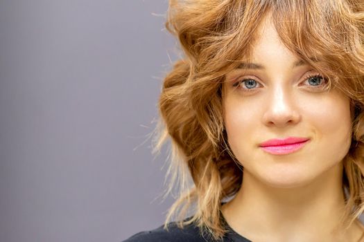 Portrait of a beautiful young caucasian red-haired woman with short wavy hairstyle smiling and looking at camera on dark gray background with copy space