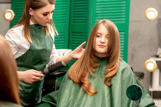 Professional hair care. Young female red-haired with long hair receiving hairstyling in a beauty salon.