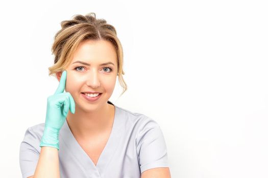 Close-up portrait of young smiling female caucasian healthcare worker standing and staring at the camera wearing gloves on white background