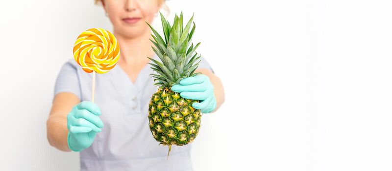 Young caucasian female doctor nutritionist holding fresh pineapple with lollipop over white background
