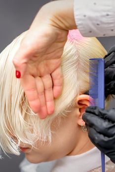 Combing hair with a comb during dyeing white hair of a young blonde woman in hairdresser salon