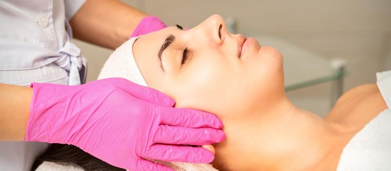 Cosmetologist with gloved hands applies a moisturizing mask with peeling cream on the female face. Facial cosmetology treatment. Procedures for facial care