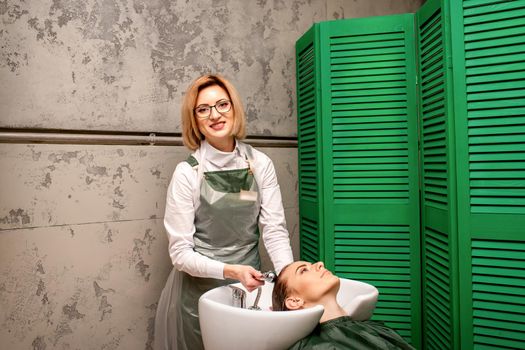 Portrait of female hairdresser washing hair of the young caucasian woman in a beauty salon