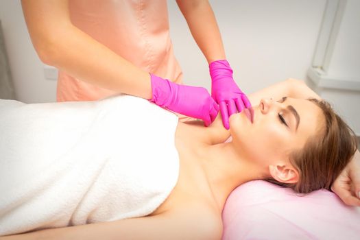 Waxing. Depilation under the armpits of the young woman lying with closed eyes in the spa salon