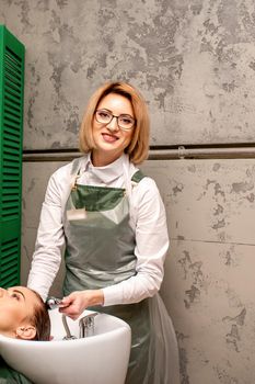 Portrait of female hairdresser washing hair of the young caucasian woman in a beauty salon