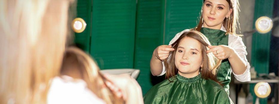 Professional hair care. Beautiful young caucasian brunette woman with long hair receiving hairstyling in a beauty salon