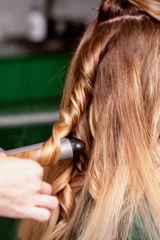 The female hairdresser is curling hair for a brown-haired young caucasian woman in a beauty salon