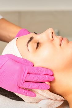 Cosmetologist with gloved hands applies a moisturizing mask with peeling cream on the female face. Facial cosmetology treatment. Procedures for facial care