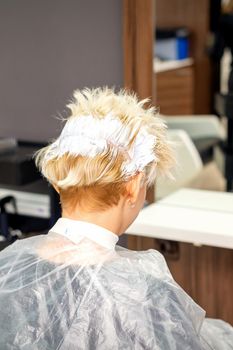 Coloring white hair with hair dye of the young caucasian blonde woman sitting at a hair salon, close up