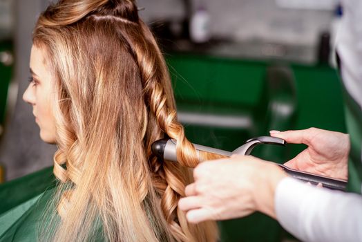 The female hairdresser is curling hair for a brown-haired young caucasian woman in a beauty salon