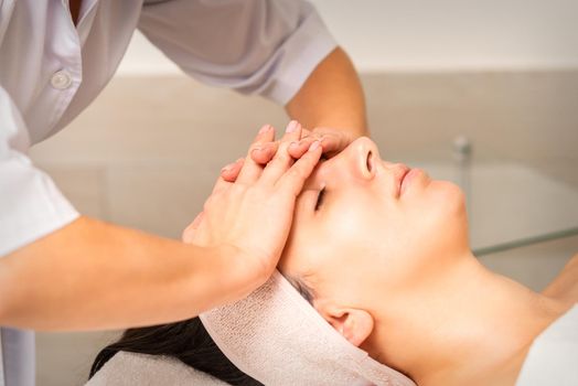 Facial massage. Young caucasian woman with closed eyes getting a massage on her forehead in a beauty salon