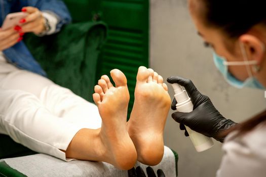 A woman getting a pedicure and pedicurist moisturizing female feet with lotion spraying in a beauty salon