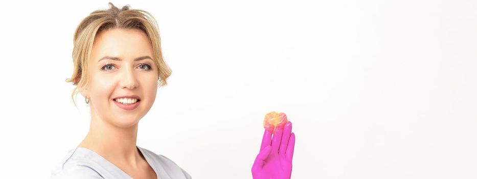 Young caucasian smiling female beautician holding wax for depilation over white background. Yellow sugar paste in hands master of depilation. Epilation concept