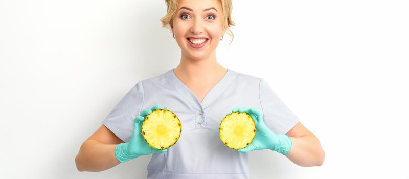 Young Caucasian smiling woman doctor nutritionist holding slices pineapple over isolated white background, breast health concept