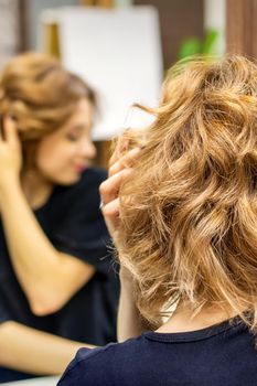 Young woman checking her new curly brown hairstyle in front of the mirror at the hairdresser salon.