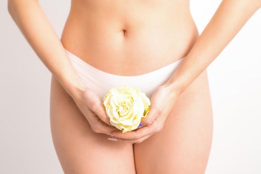 Caucasian woman in white panties with white rose flower on a uniform background, closeup