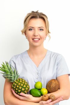 Portrait of a young caucasian smiling female nutritionist with different fruits in her hands over white background