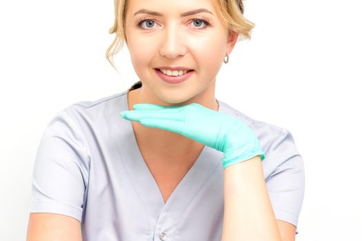 Close-up portrait of young smiling female caucasian healthcare worker standing and staring at the camera wearing gloves on white background