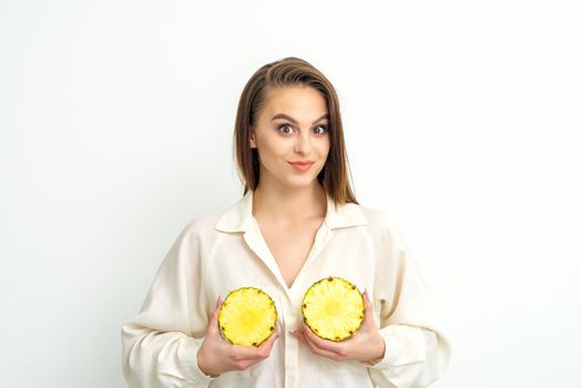 Young Caucasian smiling woman holding slices pineapple over white background, breast health concept