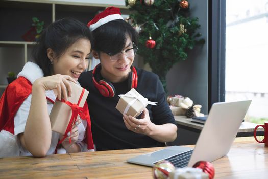 Happy asian couple holding gift box and having video call on laptop computer.