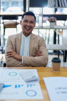 Portrait of a male business owner showing a happy smiling face as he has successfully invested his business using computers and financial budget documents at work.