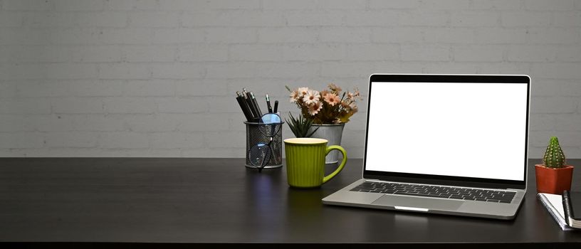 Mock up laptop computer, coffee cup and pencil holder on wooden table with brick wall.