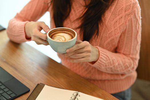 Cropped shot young woman in sweater holding cup of coffee.