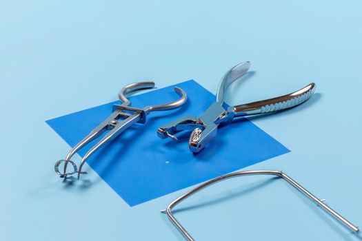 Dental hole punch, a rubber dam forceps with the clamp on the blue rubber dam and the metal frame. Medical tools concept.