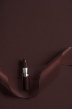 Cosmetic branding, glamour lip gloss and shopping sale concept - Luxury lipstick and silk ribbon on chocolate holiday background, make-up and cosmetics flatlay for beauty brand product design