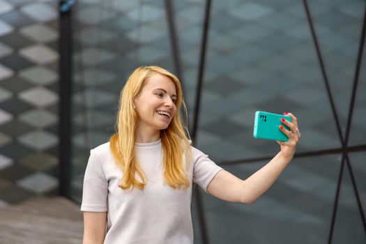 Young blond woman making selfie on smartphone for her followers. Young influencer girl. Popularity in internet, friends online. Beautiful girl making content for her social media account