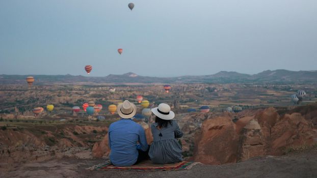 Asian women and caucasian men mid age on a trip to Kapadokya Cappadocia Turkey, a happy young couple during sunrise watching the hot air balloons of Kapadokya Cappadocia Turkey during vacation