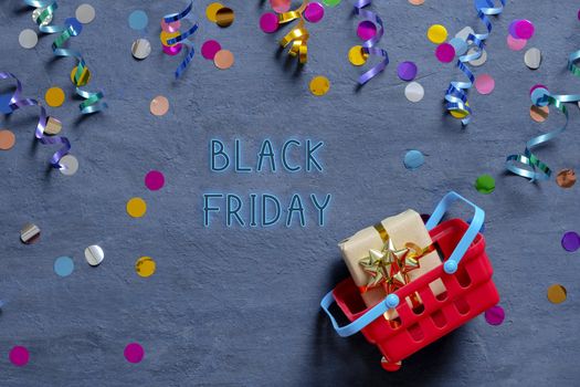 Black Friday tetx with shopping basket and festive tinsel flat lay on dark background. Top view.